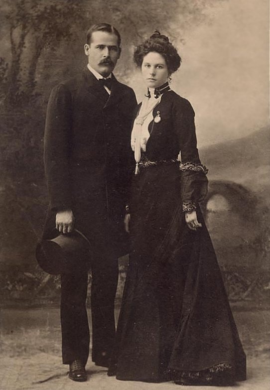 Studio portrait of Harry Longabaugh, the Sundance Kid, and Etta Place, both formally dressed. He holds a top hat; she wears a gold watch pinned to her lapel.