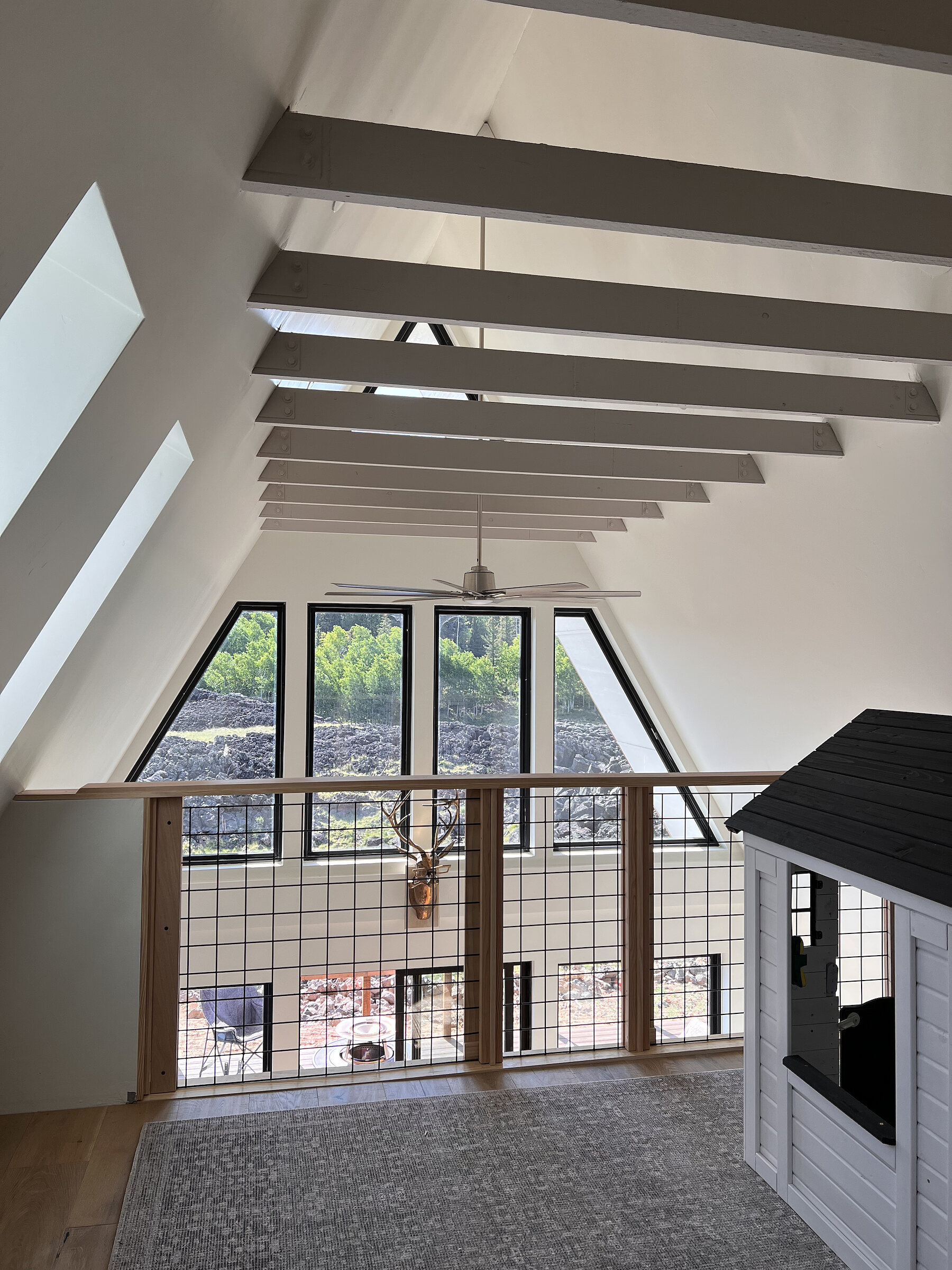 The loft looking down through the gable window, open beams overhead and a railing at the edge.